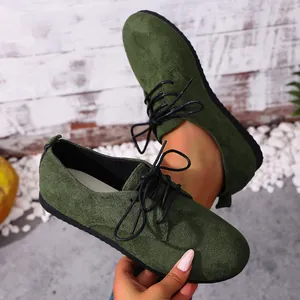 Close-up of dark green suede lace-up flat shoes for women on a rustic background