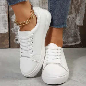 Close-up of women's white low-top sneakers with gold chain anklet detail on street