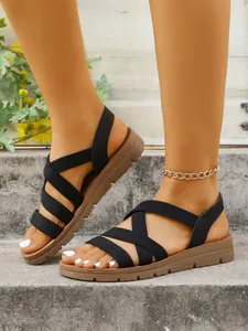 Detail of black elastic cross-strap sandals with comfortable flat brown soles.