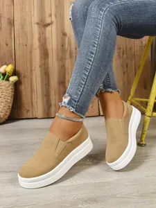 Detail of tan suede slip-on sneakers with thick white soles on a female model.