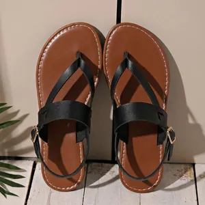 Top view of flat black and brown thong sandals with ankle straps on wood floor