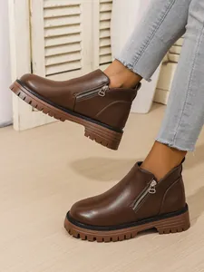 Close-up of brown leather ankle boots with thick rubber soles and side zippers worn on feet.