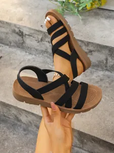 Side view detail of black elastic strap women's flat Roman sandals with brown sole