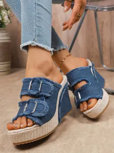 Detail view of denim wedge sandals featuring buckled straps and a woven platform.