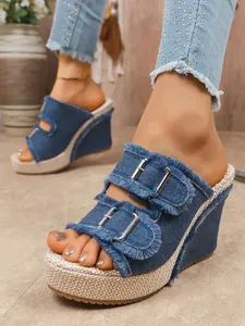 Detail shot of stylish blue denim wedge sandals with metallic buckles and fringe trim