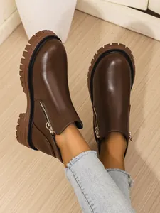 Close-up of stylish brown chunky platform ankle boots with side zippers on model.