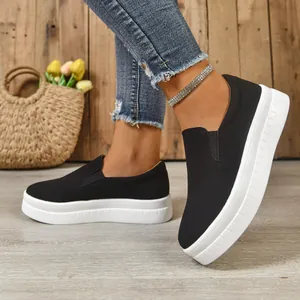 Close-up detail of black slip-on platform loafers with thick white soles on wooden floor