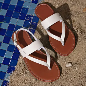 Detail view of white thong sandals with brown insoles on a sandy beach background
