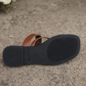 Detail showing the black non-slip textured sole and brown straps of the flat sandal.