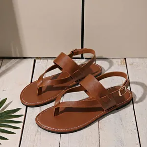 Side view of brown leather flat thong sandals with gold buckle on white wood background