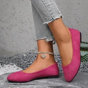 Primo piano di eleganti ballerine in camoscio fucsia con punta a punta su sfondo di pietra.