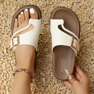 Detail shot of white asymmetric strap sandals with gold buckle and brown footbed