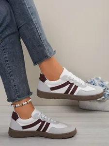 Detailed view of women's color-blocked GAT sneakers worn with jeans on a wooden floor.
