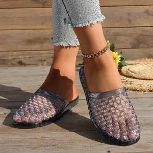 Close-up of grey hollowed-out crystal jelly slides worn on a wooden deck in sunlight.