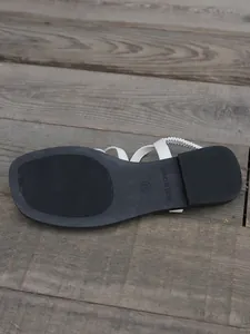 Vue détaillée de la semelle noire antidérapante des sandales plates à bride élastique blanche