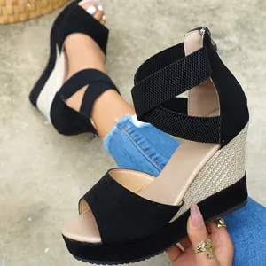 Close-up view of black suede wedge sandals featuring cross straps and woven platform