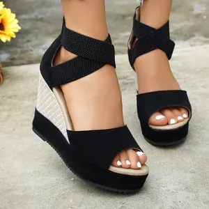Close-up of black suede wedge sandals with elastic crisscross ankle straps and platform sole