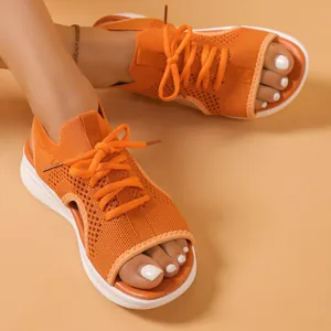 Detail view of orange fly-woven sporty sandals with white platform soles on feet