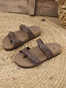 Brown women's flat sandals with belt buckles and cork textured soles on straw mat