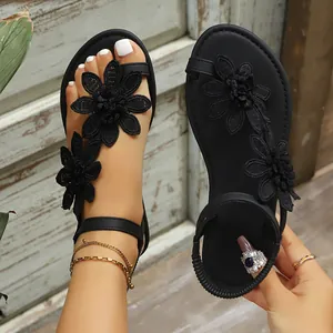 Detailed macro view of black toe-loop flat sandals with intricate lace flower accents