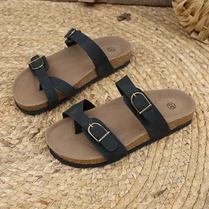 Detail view of black women's flat buckled sandals with cork footbed on a woven straw mat