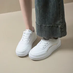 Detail view of stylish white minimalist platform sneakers with gold trim worn by a model