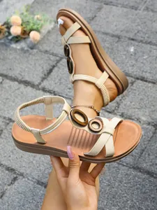 Detail shot of beige flat sandals with wooden rings and elastic heel straps.