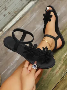 Close-up of black flat sandals with elegant 3D floral lace appliques and elastic strap