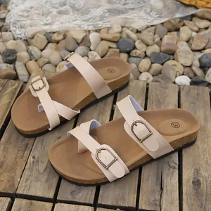 Close-up view of beige women's flat sandals with adjustable buckles on wood surface