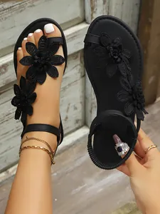 Close-up detail of black Roman sandals featuring intricate lace flower decorations.