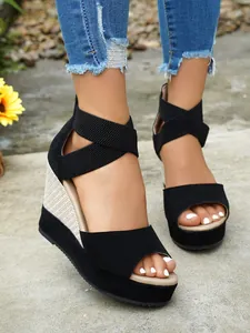 Close-up of stylish black suede wedge sandals with elastic cross straps and platform sole