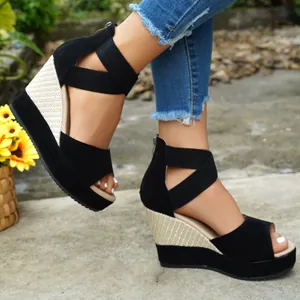Close-up of black suede wedge sandals with elastic cross straps and a straw-textured heel.