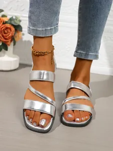 Detaillierte Ansicht der flachen römischen Sandalen in Silbermetallic mit Kreuzriemen.