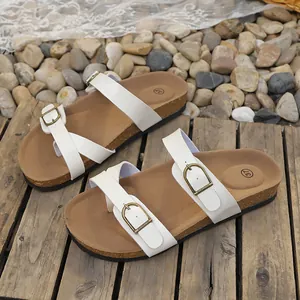Detailed view of white flat sandals featuring adjustable gold-tone metal buckles.