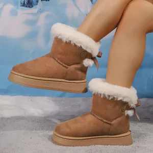 Close-up of camel snow boots with white fur lining and bow detail on snowy background.