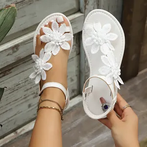 Close-up of white toe-loop flat sandals with delicate lace flower decorations