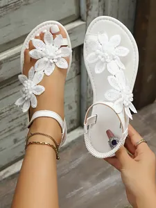 Detail view of white flat sandals with elegant lace flower appliqués and toe-post