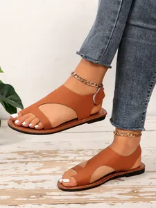Primo piano di eleganti sandali bassi marroni con chiusura a strappo e catene d'oro.