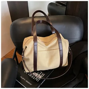Detalle de un gran bolso tote de lona caqui con correas de cuero marrón sobre silla.