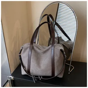 Detalle de un bolso de viaje grande de lona gris con correas de hombro marrón oscuro.