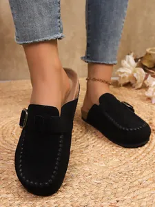 Close-up of stylish black suede platform clogs featuring metal buckle and whipstitch detail