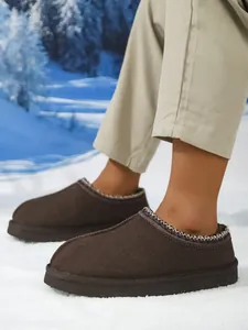 Primer plano de pantuflas de invierno marrones para hombre con ribete trenzado sobre la nieve
