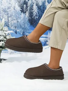 Primer plano de zapatillas cálidas marrones con cuello bordado en la nieve del exterior