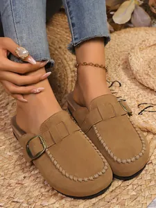 Detailed view of brown suede mules with buckle and whipstitch on straw mat
