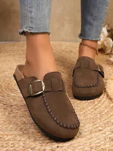 Detail view of brown suede Birkenstock-style clogs with gold buckle and stitch decor