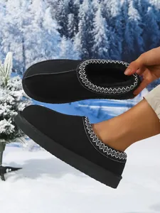 Primer plano de zapatos de nieve negros con forro polar y bordados en escena invernal
