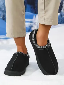 Detalle de zapatillas de invierno negras con ribete bordado blanco sobre fondo nevado