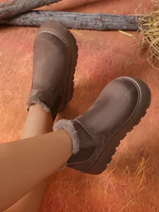 Close-up of warm brown platform snow boots with fleece lining in a rustic winter setting