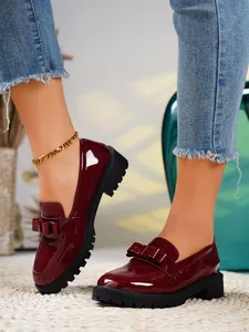 Close-up showing the glossy wine red patent leather and bow detail of loafers.