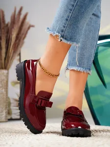 Close-up of stylish burgundy patent leather loafers with bow detail and chunky sole.